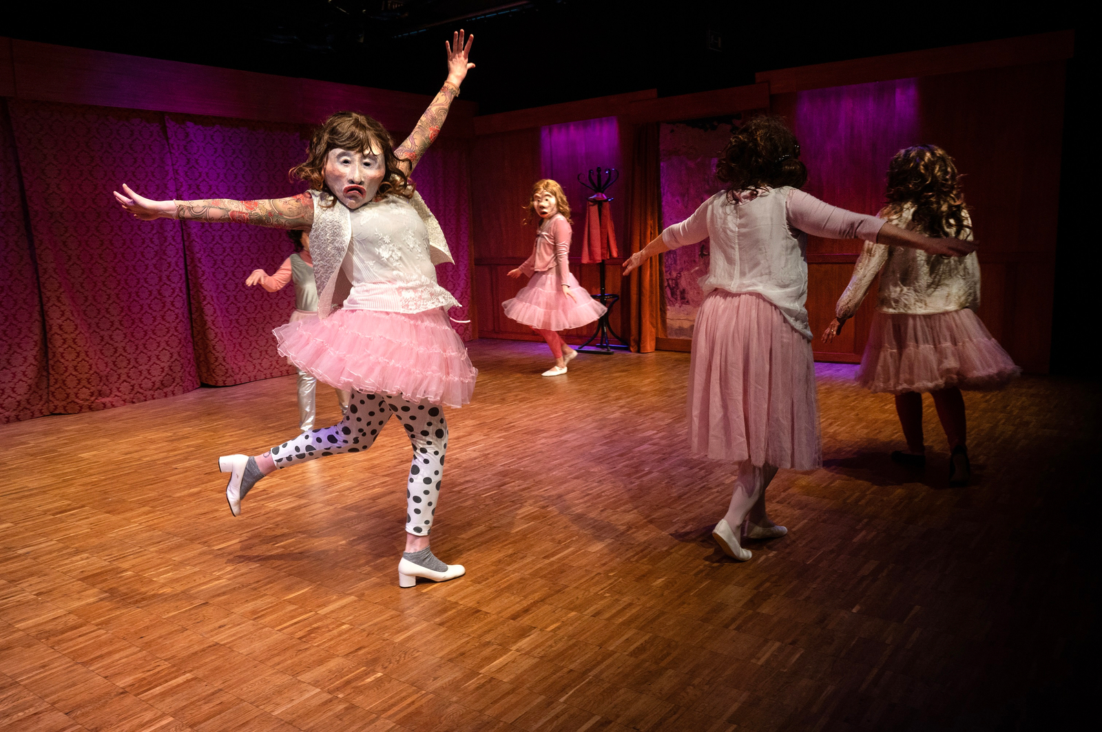 Maskentänzerinnen in rosa Balletkleidern tanzen mit ausgebreiteten Armen über die Bühne